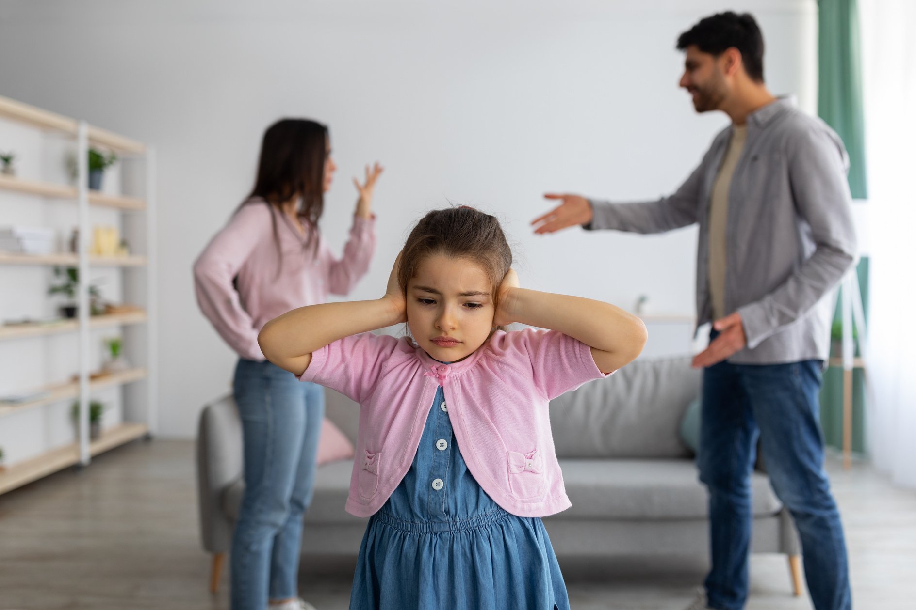 Childhood traumas concept. Upset arab girl covering ears with hands not to listen parents conflict